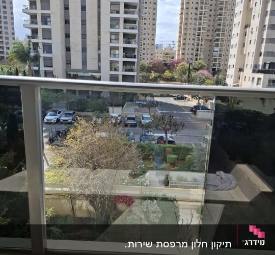מעקה זכוכית עם נוף לבניינים ועצים